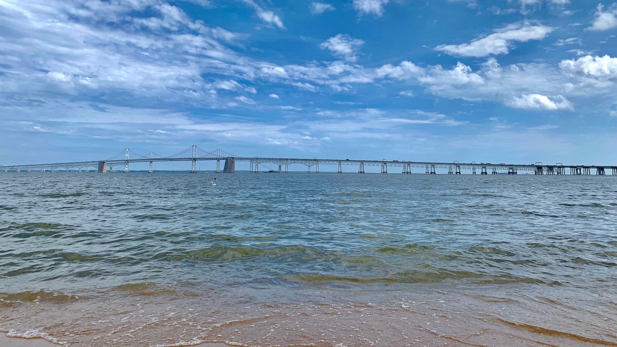 Long bridge over a body of water with a blue sky and clouds.