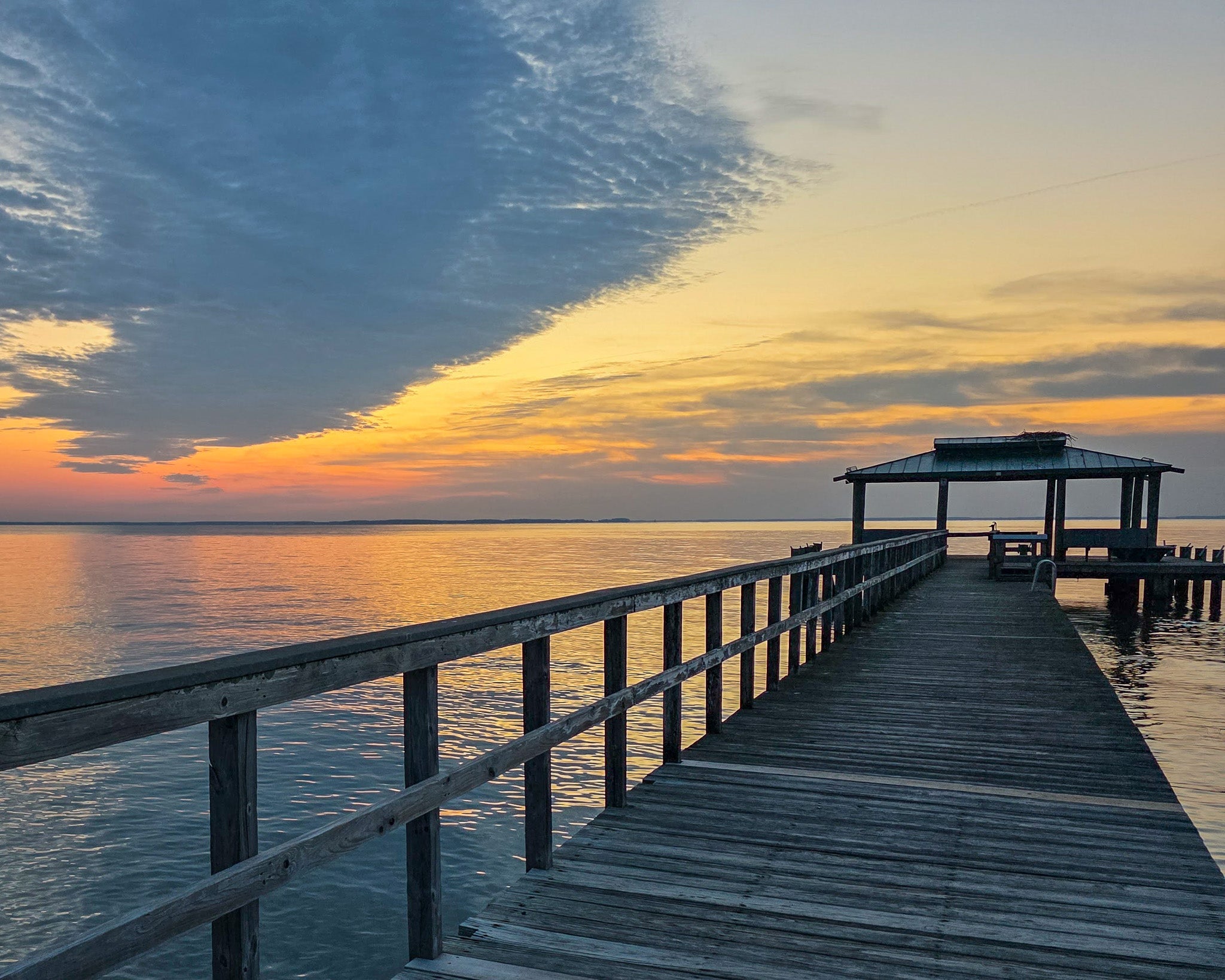 Wooden dock extending into a body of water with a colorful sunset sky.