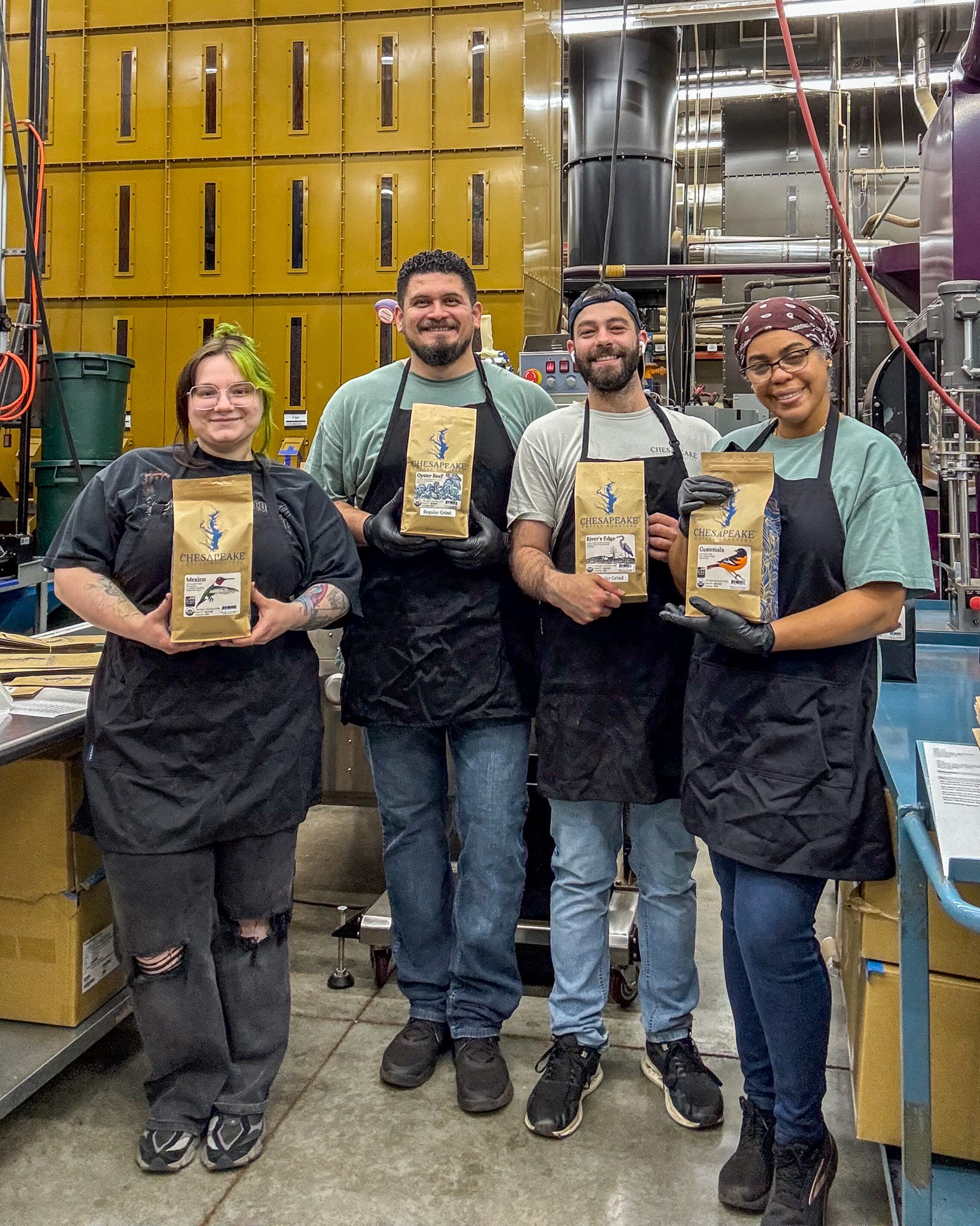 Four people in a factory setting holding bags of coffee.